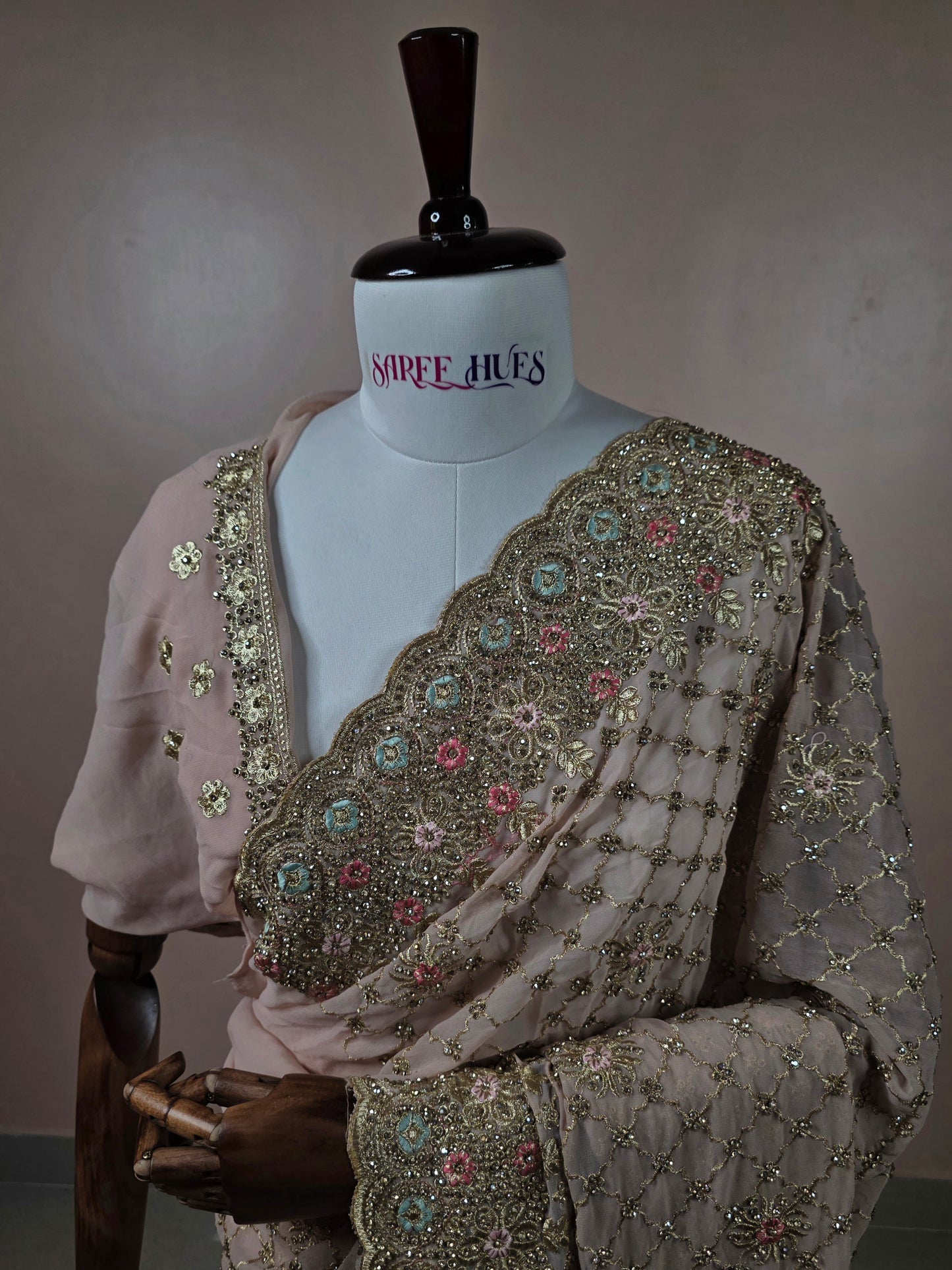 Dusty pink georgette saree with Swarovski stone jaal work and multicolor floral scalloped border on mannequin.